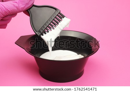 hair dye is mixed by a gloved hand in a bowl on a pink background Royalty-Free Stock Photo #1762541471