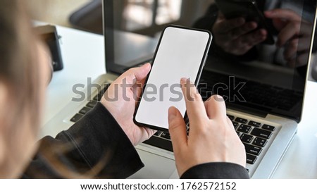 Woman using smart phone with laptop in office and hand holding smart phone empty screen.blurred background.