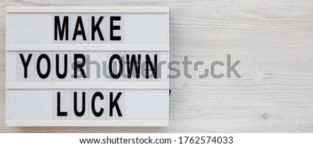 'Make your own luck' on a lightbox on a white wooden background, top view. Flat lay, from above, overhead. Copy space.