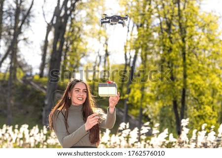 on a sunny and windy day young smiling emotional brunette receives a surprise gift delivered by quadcopter, drone delivery service, concept of modern fast delivery method