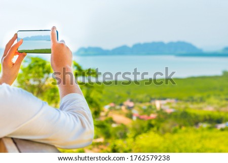 Young woman with mobile phone taking image of Thailand mountain island sea landscape