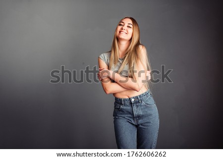Photo portrait of a beautiful smiling woman girl on a gray background in jeans and a blouse with long blond beautiful hair. Standing right in front of the camera.