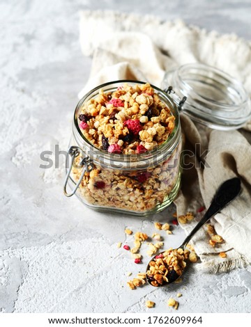 Homemade granola with berries and nuts in a glass jar on a gray background