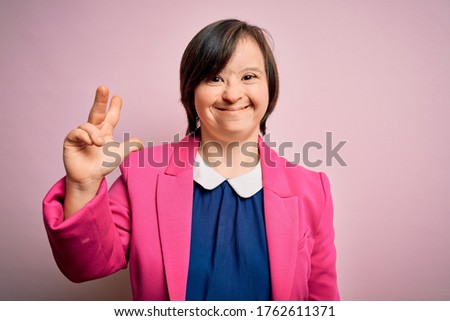 Young down syndrome business woman over pink background showing and pointing up with fingers number three while smiling confident and happy.
