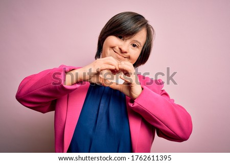 Young down syndrome business woman over pink background smiling in love doing heart symbol shape with hands. Romantic concept.