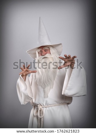 A grey-haired severe wizard in a white cassock is doing sorcery and magic against a white background.