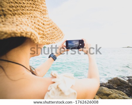 Portrait of woman who take her mobile phone to take a photo at sea in high key picture