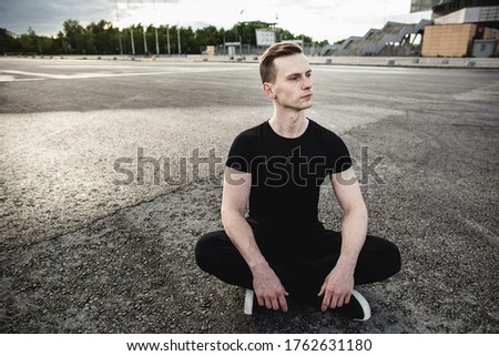 Young man sitting on the asphalt and and stretches his legs before jogging. Running, sports, healthy lifestyle. Copy space