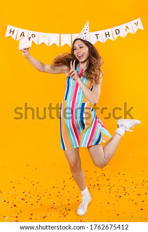 Image of joyful cute woman taking selfie on mobile phone and gesturing peace sign isolated over yellow background