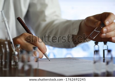A man signs a medical document. Medical equipment on the table. Stethoscope and ampoules with syringes. Makes notes in office. Medical center.