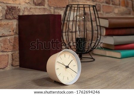 Decorative items standing on the table in the form of a table clock, books, a modern candle holder with an incandescent lamp Royalty-Free Stock Photo #1762694246