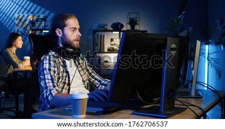 Picture of professional video editor editing video on his personal computer with two displays in modern video studio. Young man works with headphones