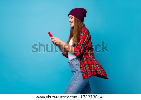 Profile side view portrait of nice attractive cute pretty cheerful focused long-haired girl wearing checked shirt using device chatting isolated over bright vivid shine vibrant blue color background