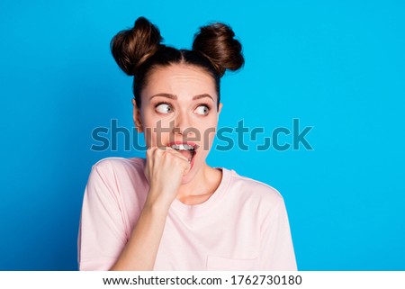 Closeup photo of attractive scared lady two buns biting teeth fingers fist look side empty space feel guilty terrified wear casual white pink t-shirt isolated bright blue color background