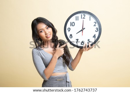 Young Asian woman point to a clock   on beige background