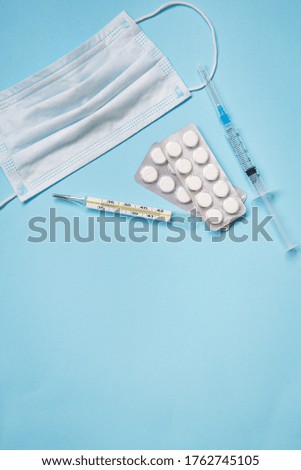On a blue background are pills, a medical mask, a thermometer and a syringe. The concept of health and self-control for viruses and epidemics. Close-up.