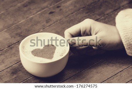 woman holding hot cup of coffee, with heart shape. Photo in old color image style.