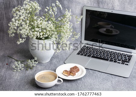 Silver laptop, vase with white flowers, a cup of coffee

