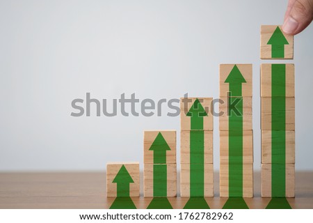Hand putting wooden cubes block which print screen increase or up green arrow. It is symbol of economic investment profit growth.
