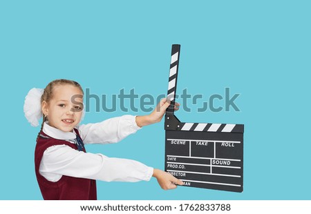 School girl with empty black filmmaking clapperboard on blue color background.