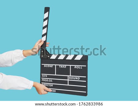 Child hands with empty black filmmaking clapperboard on blue color background.