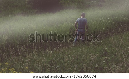 A mysterious male figure walking away in a foggy field in summer with a dark muted edit.
