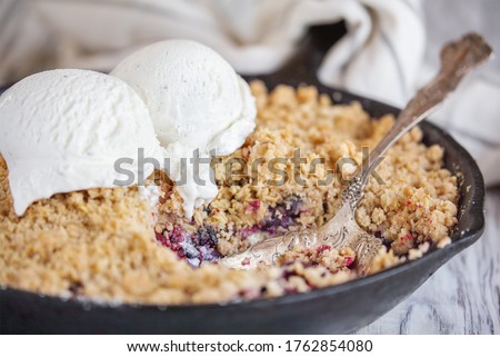 Blackberry and Blueberry Cobbler baked in a cast iron pan and topped with a golden oatmeal crisp with ice cream over a rustic white wood table. Extreme selective focus with blurred background.
