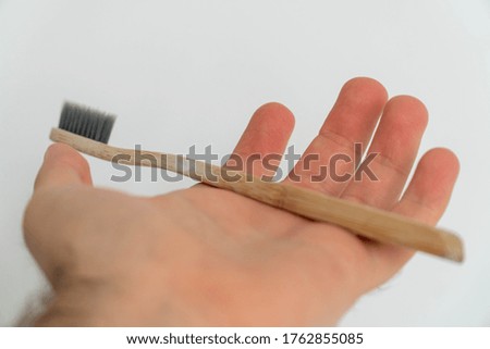 Person holding a brown bamboo toothbrush against a white wall