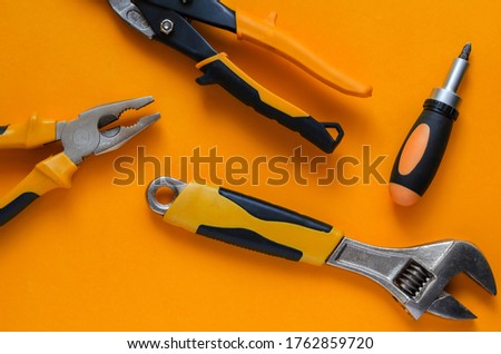 Creative background with hand tools. Hand tool with black and orange handles on an orange background. Pliers, screwdriver, adjustable wrench and scissors for cutting metal. View from above.