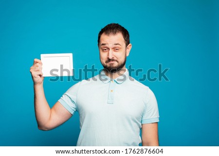 A handsome man holds a white frame with mock up in his hand and rejoices and screams, having fun