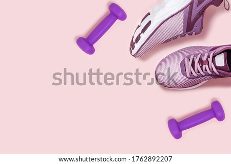 Sneakers and dumbbels on pink background. Flat lay picture.
