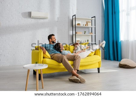 Smiling woman lying near handsome man on yellow couch at home Royalty-Free Stock Photo #1762894064