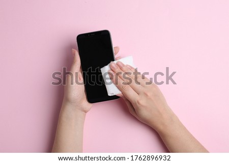 Woman cleaning mobile phone with antiseptic wipe on pink background, top view