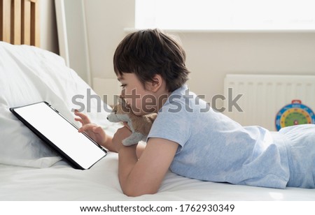 6-7 year old boy playing with dog toy and watching cartoon on tablet,Happy child lying in bed playing game in the morning, Cute Kid having fun and relaxing on his own in bed room,New normal lifestyle 