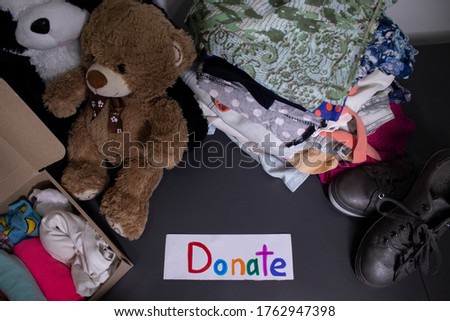 'Donate' sign handwritten with multicoloured letters. A box with clothes and a pile of clothes nearby on a grey table.clothes donation concept. copy space. High quality photo