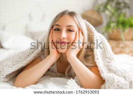 beautiful young woman lies on the bed under the covers