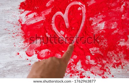 Finger painting a heart on red powder. Love concept