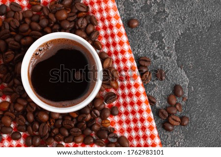 White ceramic coffee cup on checkered napkin with roasted beans
