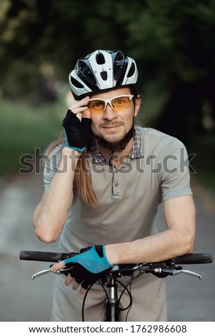 Portrait of man in a yellow sunglasses and helmet standing with bicycle on road and looking into camera. High quality