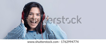 A young girl in a striped vest is listening to music in red headphones in a studio and dancing.