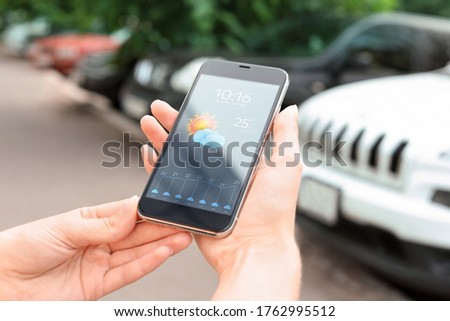 Woman using weather forecast app on smartphone outdoors, closeup