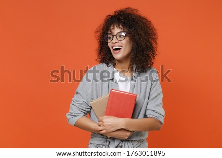 Funny young african american student girl in gray casual clothes, eyeglasses isolated on orange background studio portrait. People lifestyle concept. Mock up copy space. Hold books, looking aside