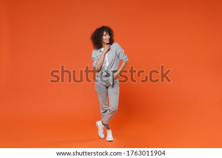 Smiling young african american woman girl in gray casual clothes posing isolated on orange background in studio. People lifestyle concept. Mock up copy space. Put hand prop up on chin, looking aside Royalty-Free Stock Photo #1763011904