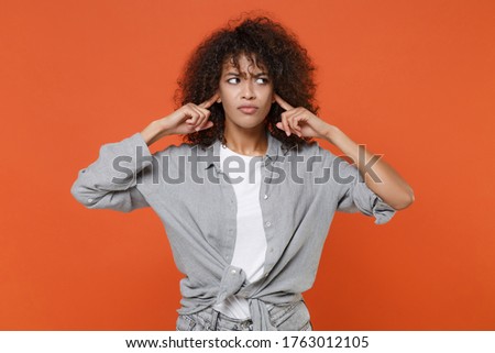 Dissatisfied young african american woman girl in gray casual clothes posing isolated on orange background studio portrait. People lifestyle concept. Mock up copy space. Covering ears with fingers