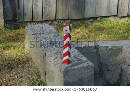 one striped iron pole limiter with a reflector on a gray concrete block on the street by the road