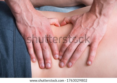 Physical therapist is making some deep massage on a mans lower back by pressing hard with thumbs.