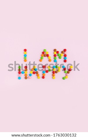 Phrase I am happy made of multi-colored chocolate candies on pink background. The concept of positive thinking. Vertical card, lay out, top view