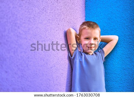 portrait of a six year old smiling boy in a blue t-shirt against the background of the wall of Violet and blue