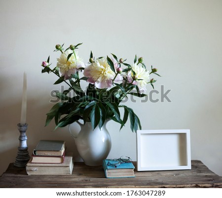 vintage interior,stillife on the table against wall with bouquet of peonies, books,and candlestick and the frame for the photo or picture