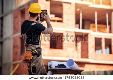 Business, building, paperwork and people concept-back view of engineer standing on construction site, take picture with tablet.